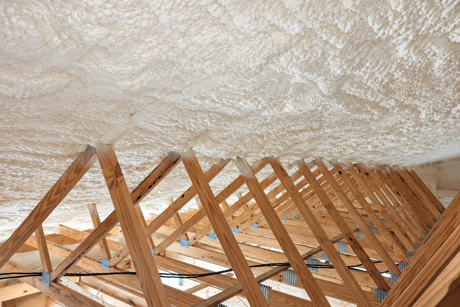 Attic roof framing with thick white spray foam coating the underside of the roof.