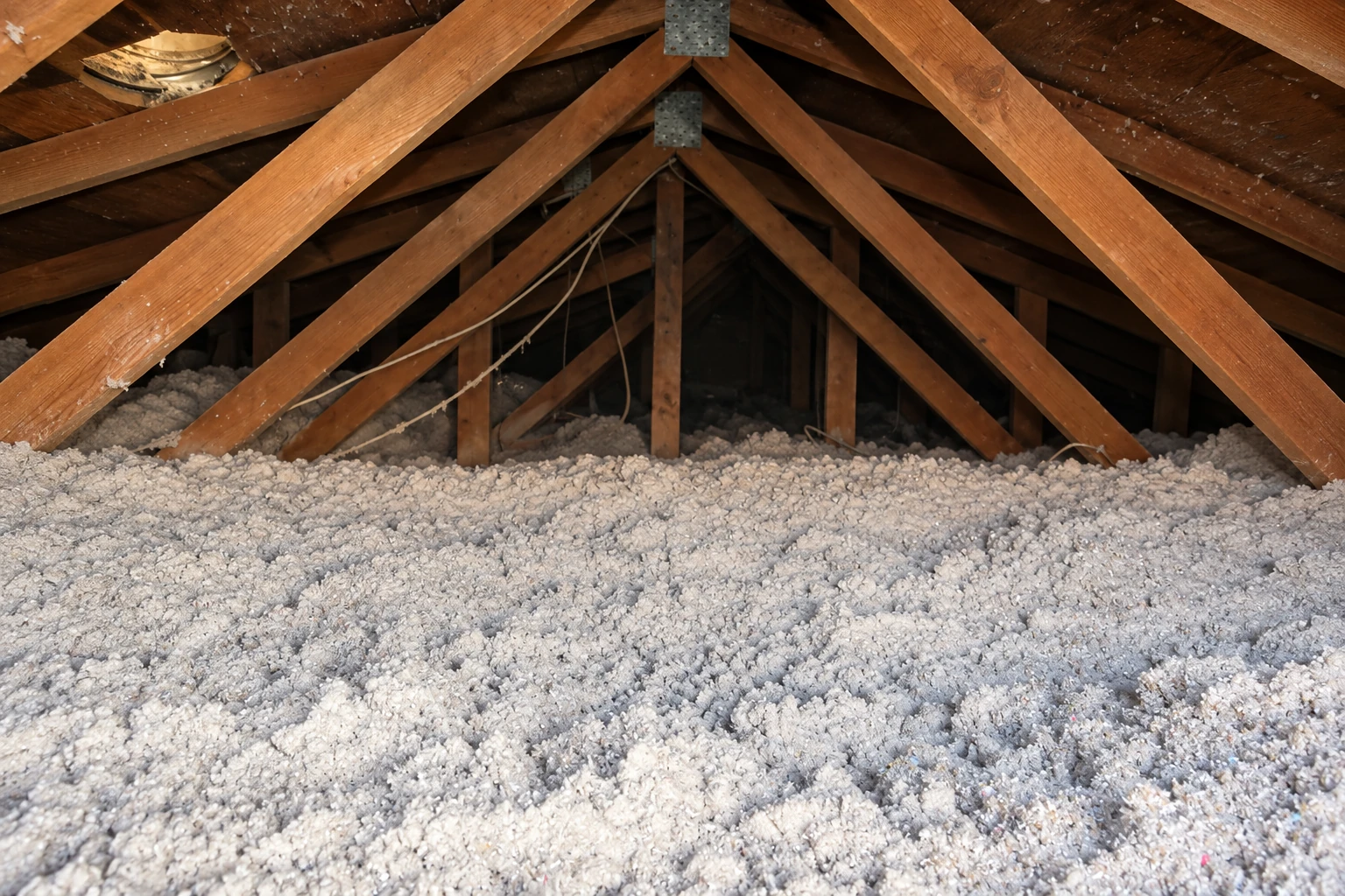 Loose-fill insulation covers the floor beneath the wooden rafters of an attic.