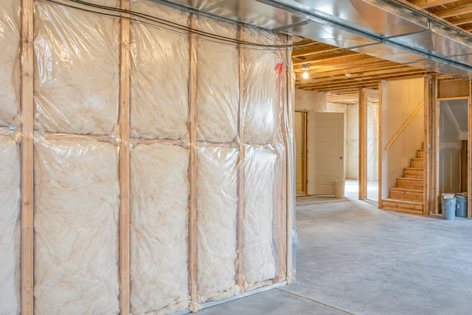 Basement with fiberglass insulation behind clear plastic on the framed walls, beneath exposed joists and ductwork.