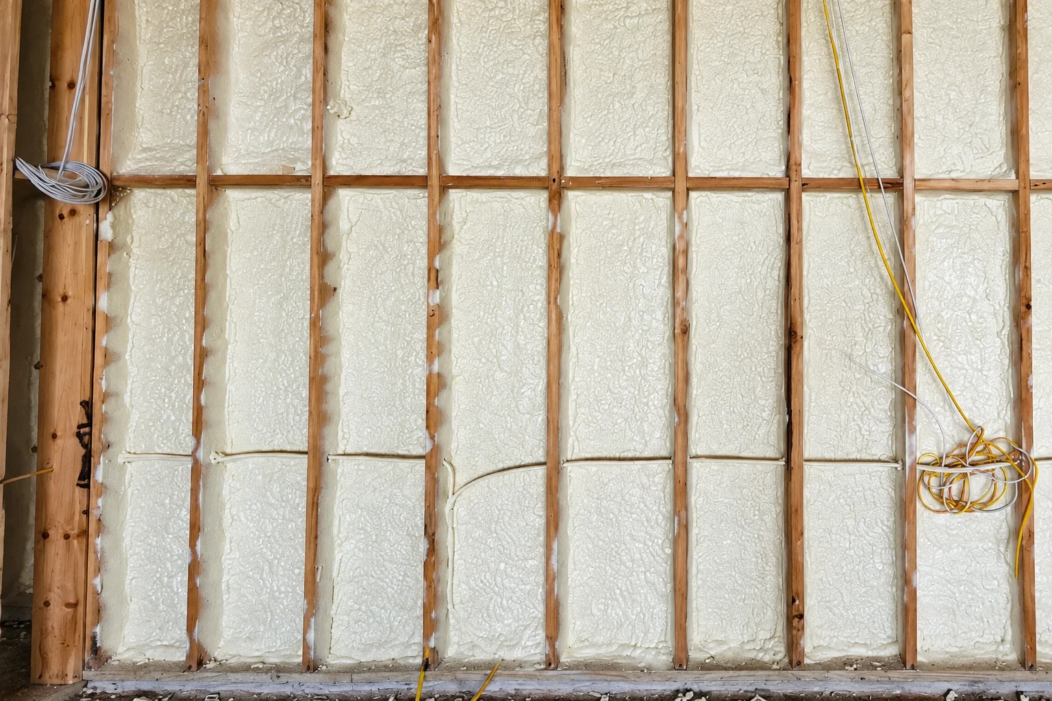 Spray foam fills the wall cavities between exposed wooden studs, with loose electrical wiring visible.