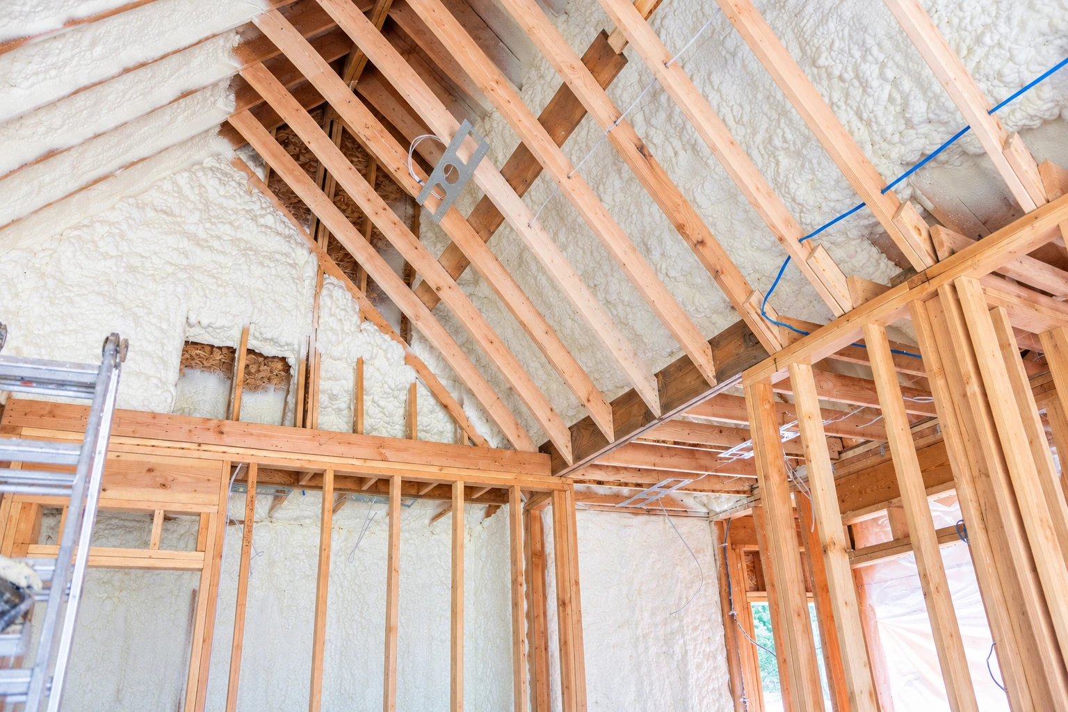 White spray foam fills the roof and wall cavities of an unfinished home framed with exposed wooden rafters and studs.